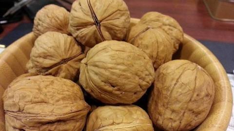 A wooden bowl of whole walnuts in their shells