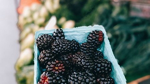 A punnet of blackberries held in a hand at a market